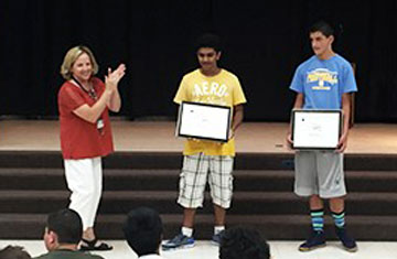 Image shows two students being aplauded by a teacher and a crowd for their project