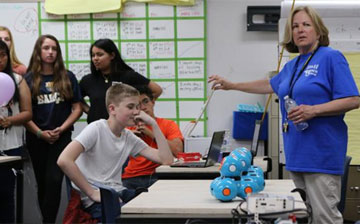 Image shows a young student looking at a small robot as a teacher explains their use