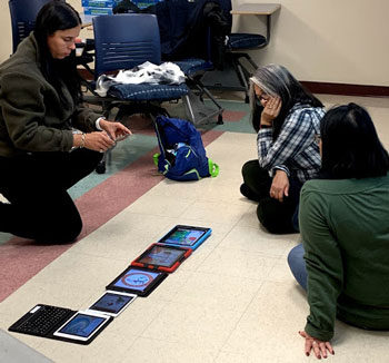 Image shows 3 female educators sitting down on the floor and looking at multiple tablets