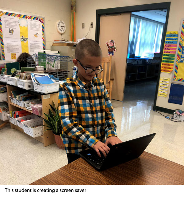 A student is standing in front of a computer typing. He is creating a screen saver.