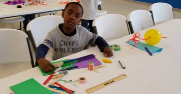 Image shows a young boy working with papers and markers in the maker space